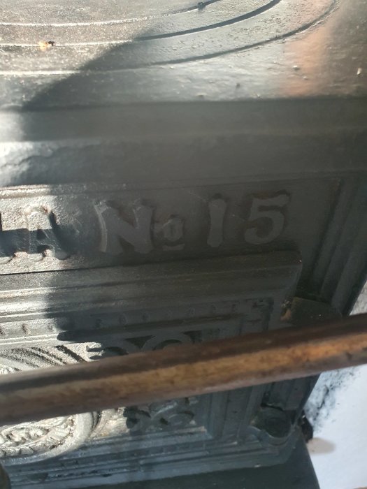 Närbild av en svart gjutjärnskamin med numret "No 15" i relief och synliga rostiga detaljer.