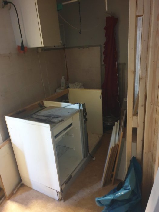 Ett halvt söndermonterat vitt kylskåp bredvid bråte och byggmaterial i ett orenoverat utrymme.