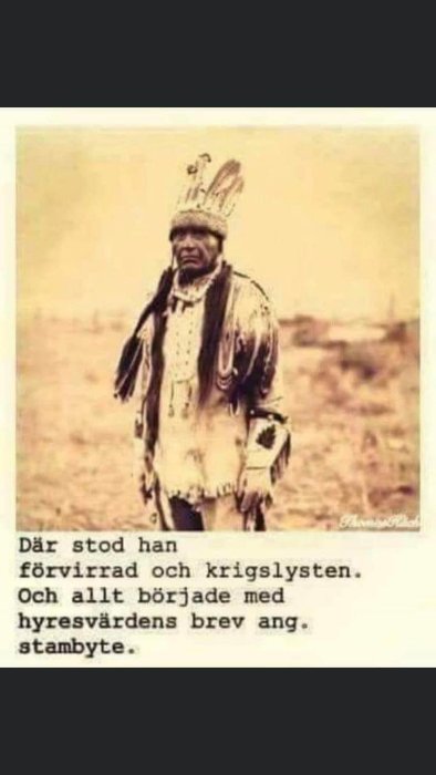 Svartvit bild av en person klädd i traditionell amerikansk ursprungsbefolkningdräkt stående utomhus.