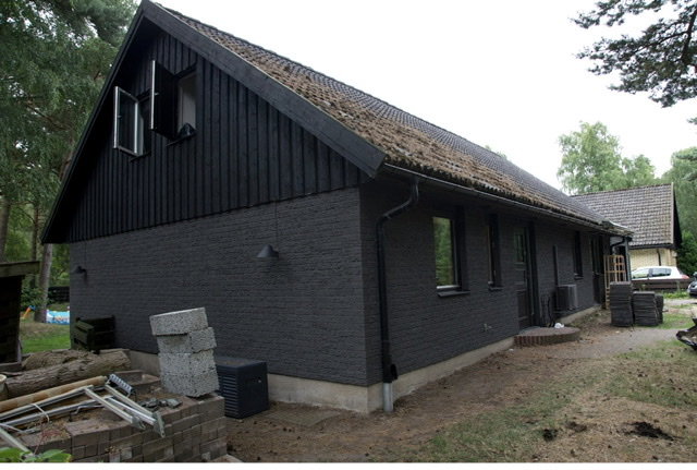 Ett hus med nyrenoverad svart fasad och vita fönster, byggmaterial syns i förgrunden.