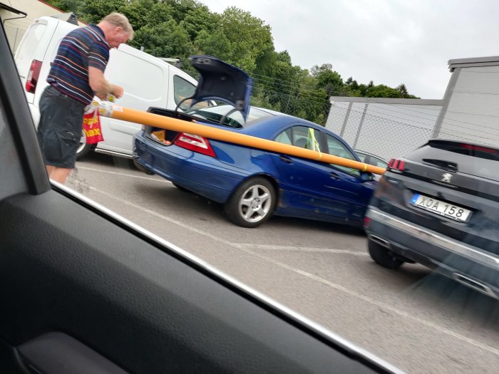 Bil med lång orange last obundet sträckande sig ut från bakluckan på en parkeringsplats.