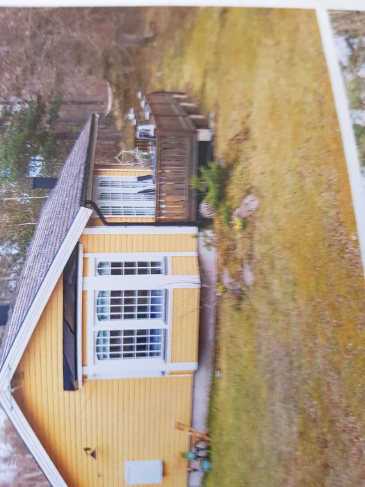 Översiktsbild från ovan på ett hus med gult träfasad och sadeltak, samt en veranda med flera fönster.