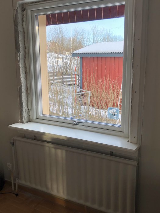 Radiator under ett fönster med synlig temperaturmätare och avskalade väggar.