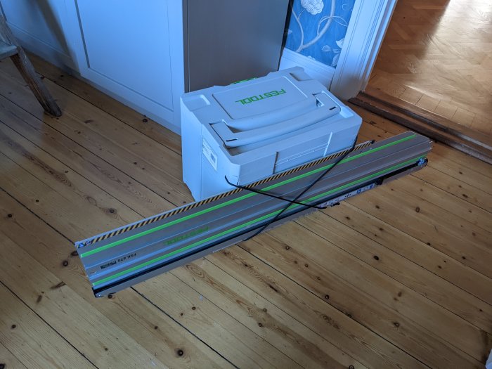 Festool systainer med gummiband som håller en lång FSK670 sågskena på ett trägolv.