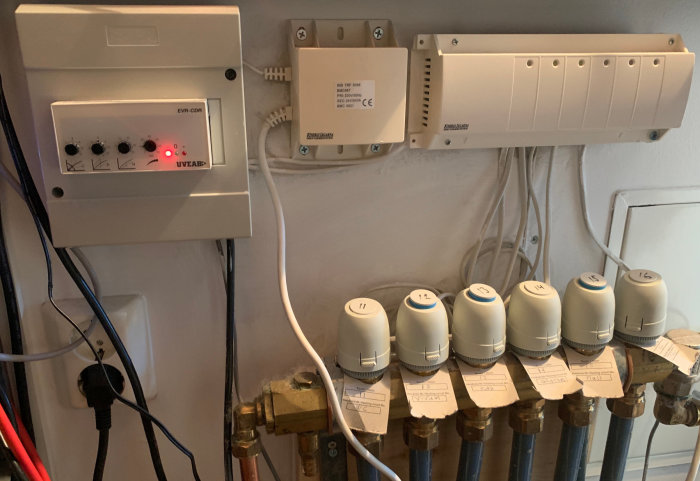 Kontrollsystem för golvvärme med ventiler och termostater på en vägg.