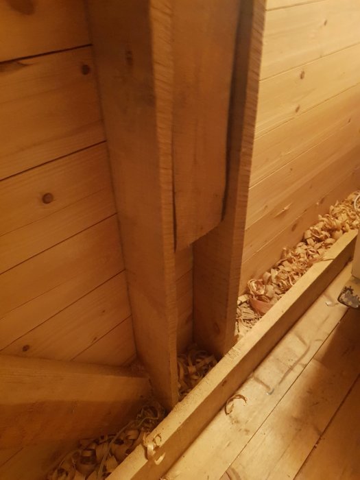 Träbjälkar i en konstruktion med spån på golvet, visar dimensioner relaterade till ett byggprojekt.