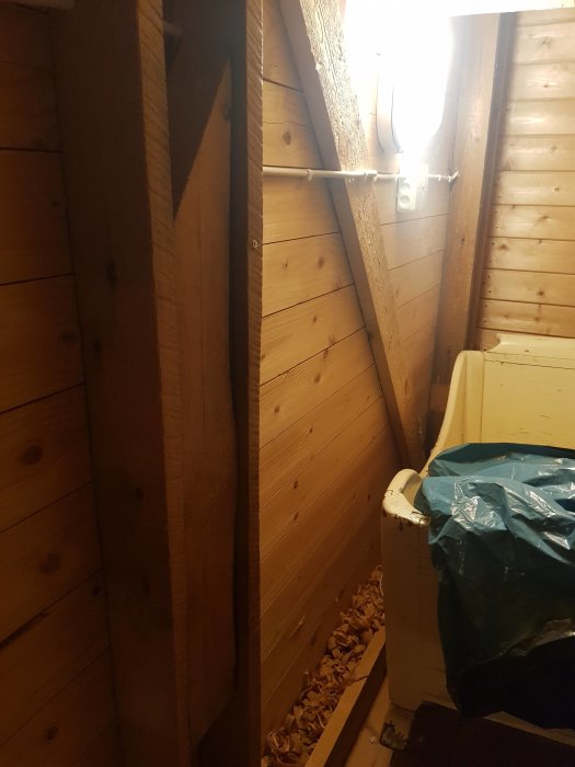 Träräkenskap av balkar i ett hörn av ett rum med synlig elinstallation och spån i en hink.