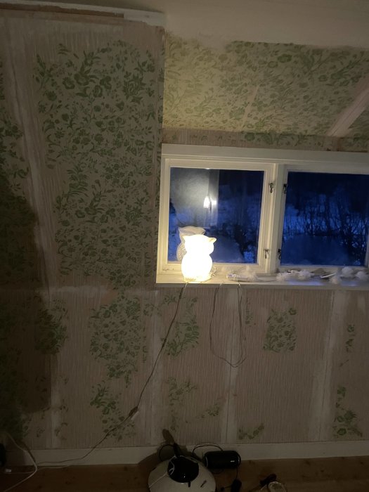 Renoveringsprojekt av ett gammalt rum med avskalad blommig tapet och synliga väggstrukturer.