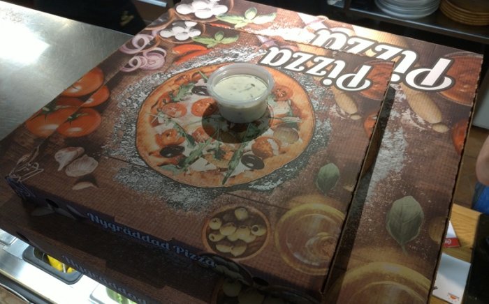 Pizzakartong med tryckt bild av pizza och en liten behållare med sås ovanpå.
