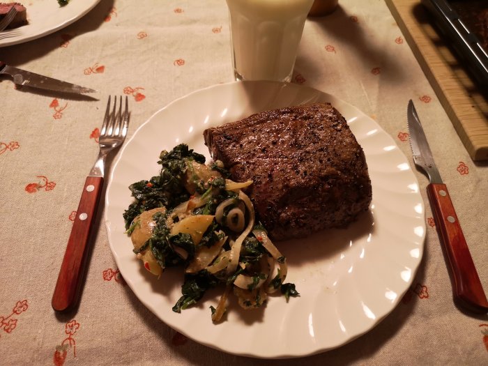 Stekt köttbit vid sidan av potatis, lök och spenat på en vit tallrik.