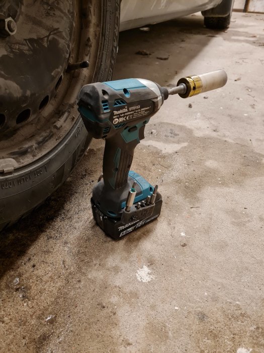 Makita slagskruvdragare med adapter vid bilens hjul under däckbyte på betonggolv.