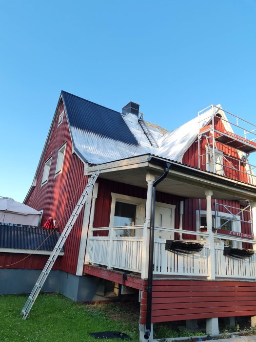 Rött trähus med nytt plåttak under konstruktion och en stege lutad mot fasaden.