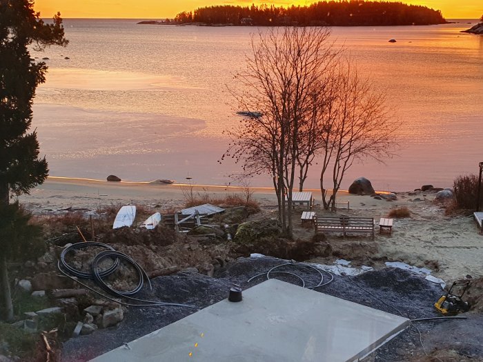 Grundläggning för utekök vid solnedgång med utsikt över ett fruset hav och strand.