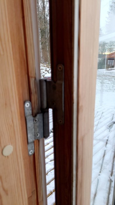 Gångjärn mellan två öppna träfönsterdörrar med utsikt mot ett snötäckt landskap.