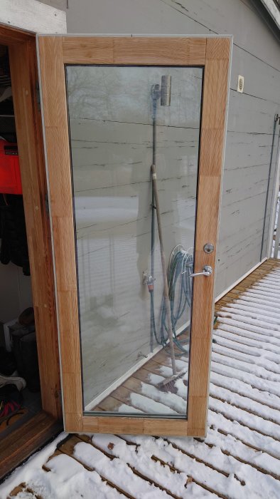 Glaspärla monterad på träram med synliga ytterdörrhandtag och lås, utsikt till snötäckt däck.