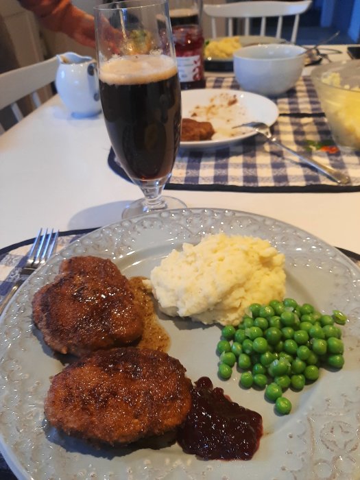 Middagstallrik med köttbullar, potatismos, gröna ärtor och lingonsylt vid ett bord.