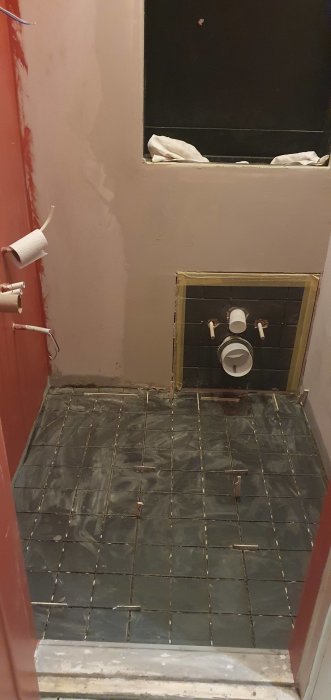 Renovering av badrum med avtäckt toalettstomme och svarta kakelplattor på golvet.