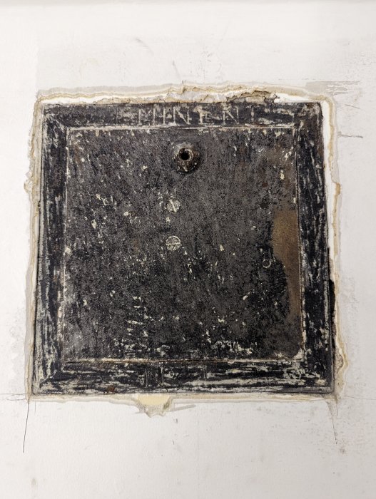 En gammal ventilkåpa som blottats efter borttagning av tapeter, i behov av restaurering.