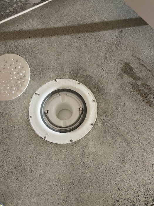 Slipat betonggolv i tvättstuga med synlig Purus golvbrunn och kakelbård.