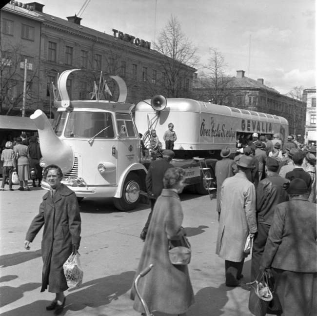 Volkswagen-lastbil formad som kaffepanna med Gevalia-reklam omgiven av människor på 1950-talet.