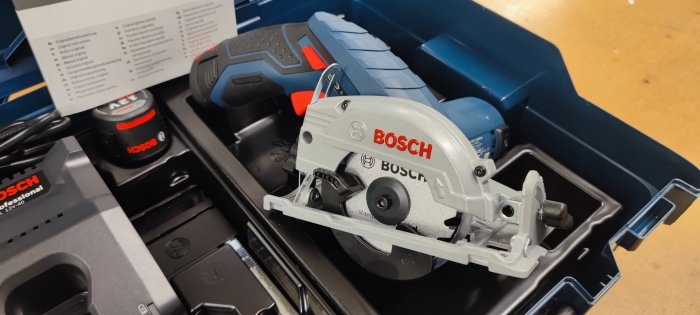 Ny Bosch cirkelsåg i blå förvaringslåda med batteri och bruksanvisning synliga.