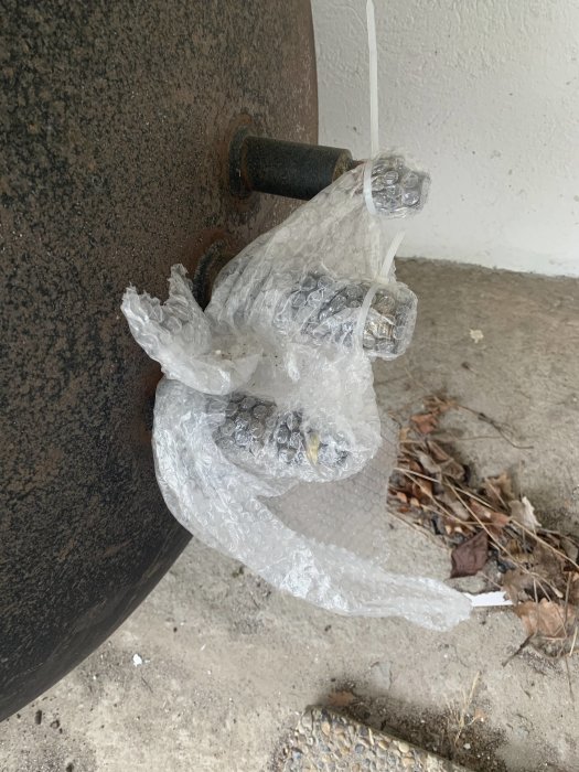 Bubbelplast inslagen runt en brunstensvikt på betonggolv med löv, oplacerat för avhämtning.