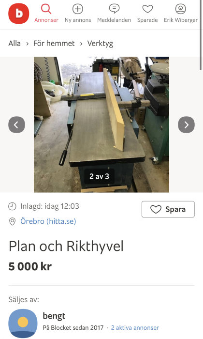 Träplanka på en plan- och rikthyvel i verkstadsmiljö, med verktyg i bakgrunden.