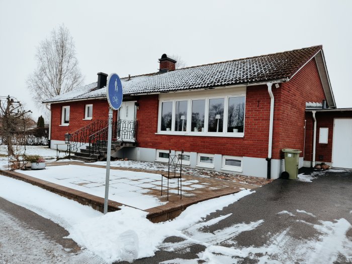 Rödtegelfasad enskilda bostadshus med snö på taket och marken, grå fönsterkarmar och vit grund.