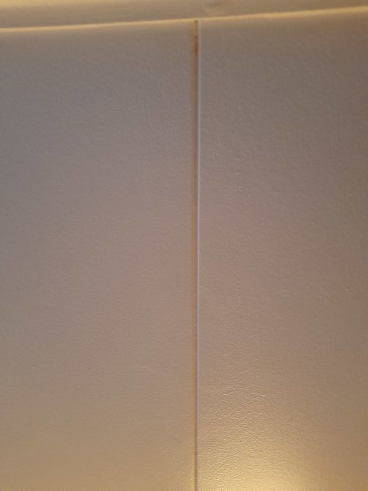 Närbild av en beige vägg med tydlig skarv mellan två väggpaneler under belysning.