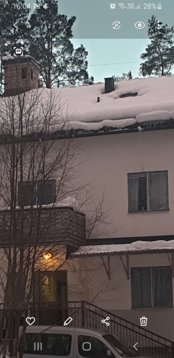 Tak med snö och ventilationstrumma nära igensatt fönster på husfasaden.