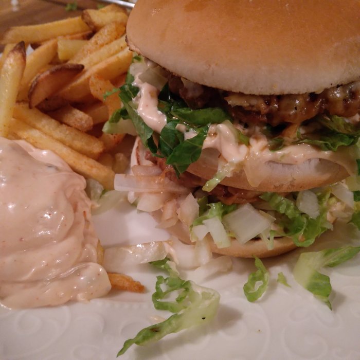 Hemlagad dubbel cheeseburgare med sallad och dressing, serverad med pommes frites och extra sås.