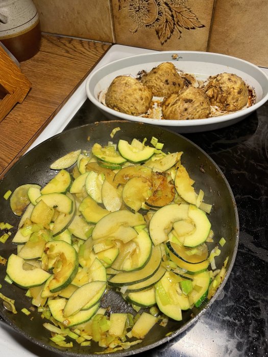 Bakade rotselleriknölar i form och frästa zucchini och purjolök i stekpanna på köksbänk.