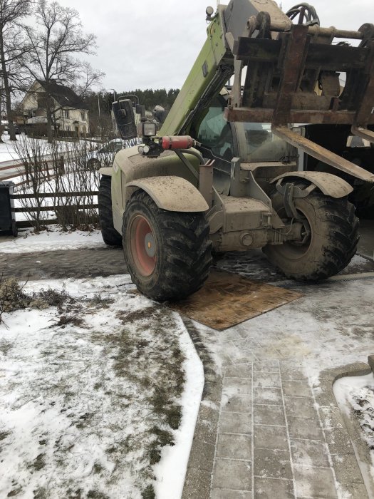 Teleskoplastare med gafflar på en tillfällig ramp av träplankor för byggprojekt på en grusig yta med snö.