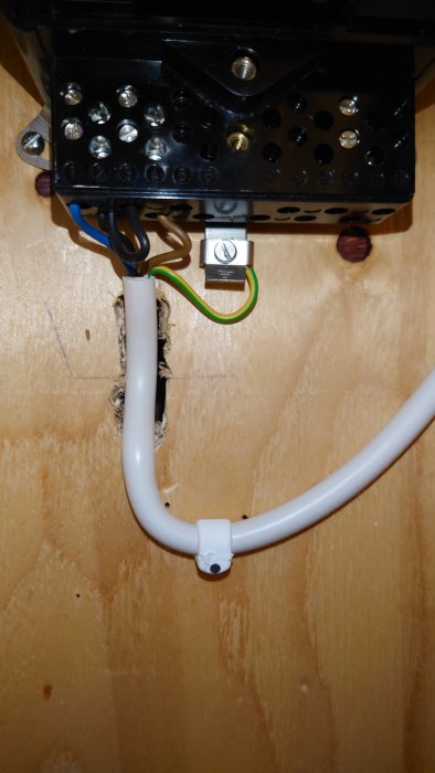 Elektrisk anslutning med kablar i en kopplingsdosa och genomföring i vägg, installationsdetaljer synliga.