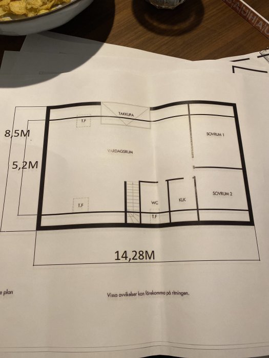 Ritning av en husplan med måttangivelser för vardagsrum, sovrum, WC, och takkupa.