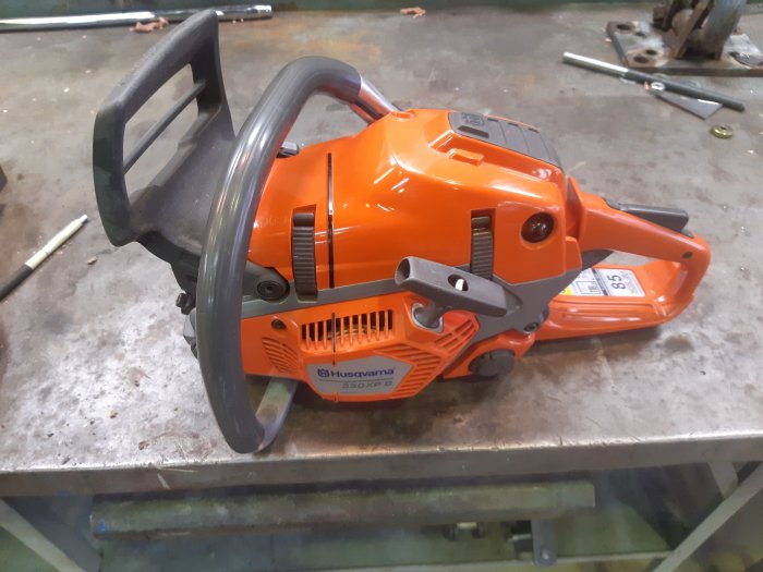 Ren och snygg orange motorsåg av märket Husqvarna upplagd på en metallbänk i en verkstad.