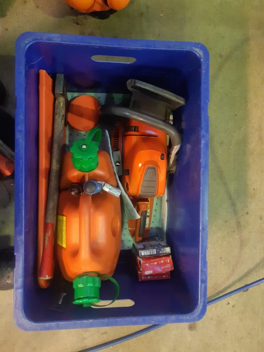 Motorsåg och skogshuggarutrustning packade i en blå plastback inkluderar hjälm, yxa och soppadunk.