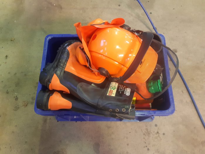 Skogshjälm, stövlar och övrig skogsarbetarutrustning packade i en blå plastback.