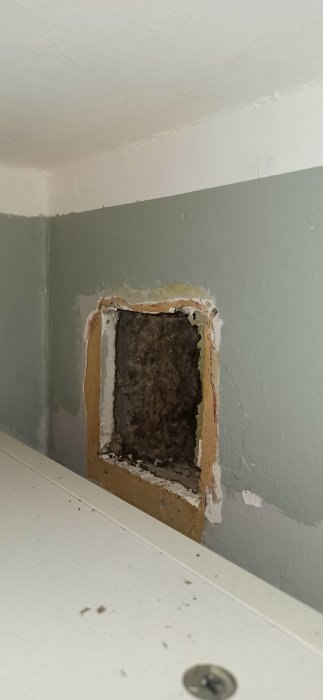 Öppet ventilationshål på 120mm i en vägg med synliga isoleringsmaterial och avskalad färg.