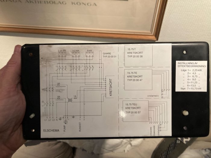 Hand håller en svart plastplatta med kopplingsschema för ett kretskort.