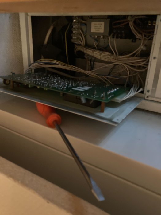 Baksidan av ett kretskort med många kablar och en skruvmejsel, inuti en elcentral.