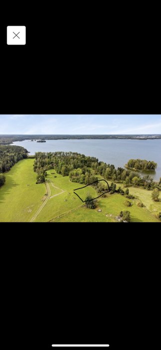 Flygbild över landskap med markerad tomt nära en sjö och omgivande grönområden.