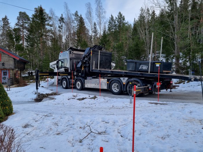 Lastbil med kran som just har nedmonterat en skorsten, parkerad vid ett hus med snö omkring.