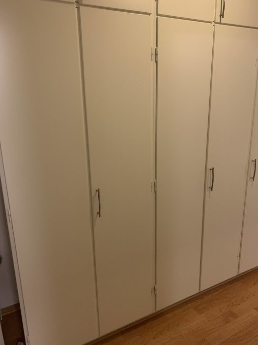 Flera vita inbyggda garderobsdörrar med handtag i ett hem.