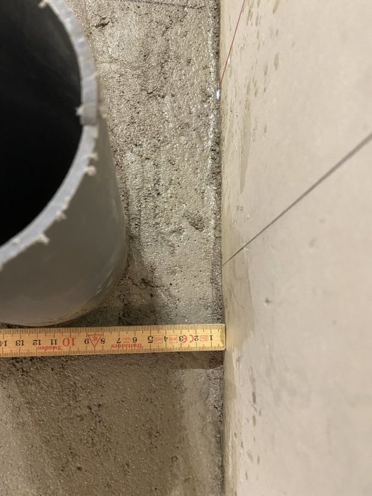 Nygjutet golv med måttband som visar höjdskillnaden mellan avloppsrör och golvnivå.