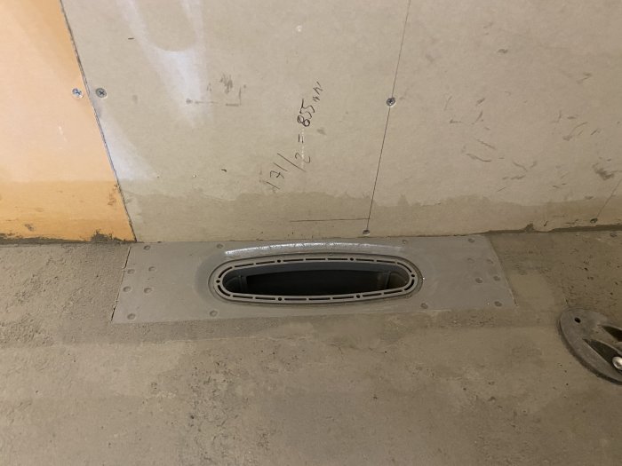 Gjutet golv med golvbrunn nära en vägg visande detaljer av tätskiktet och installationshöjd.