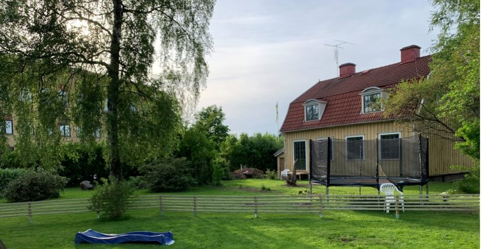 Trädgård med nytt staket 10cm in på tomten, trähus i bakgrunden och studsmatta framför.