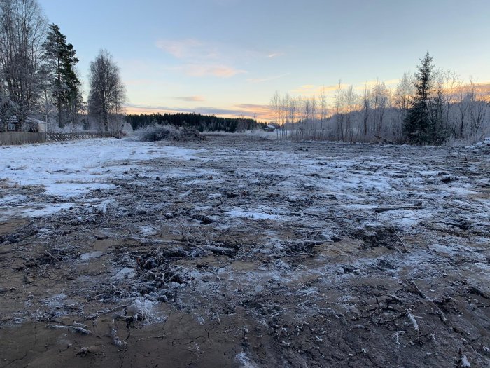 Tomt med uppgrävd jord och snörester, skymningshimmel i bakgrunden.