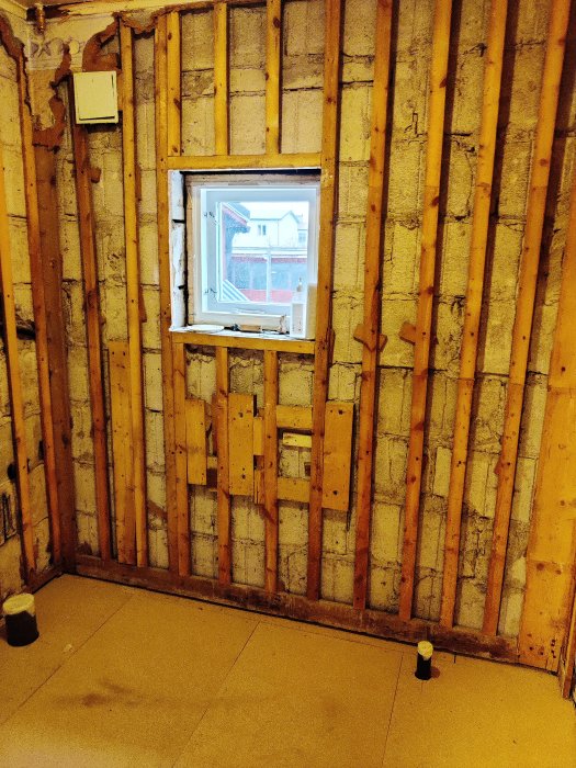 Renoverat badrum med blottlagda träreglar och isolering i väggar, synliga rör och renoverat golv.