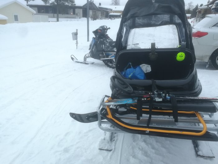 Snöskoter framför med släde och skidor, andra skoter i bakgrunden, vinterscen med snö.